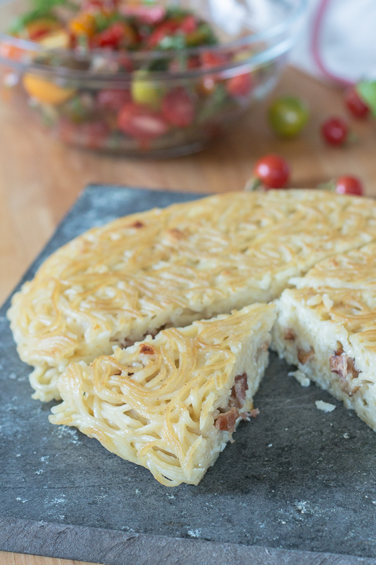 With bacon and cheese tucked in the center, this savory noodle cake tastes delicious topped with fresh summer tomatoes. This simple, flavorful recipe is easy to prepare. It's a great way to use up leftover spaghetti, too!